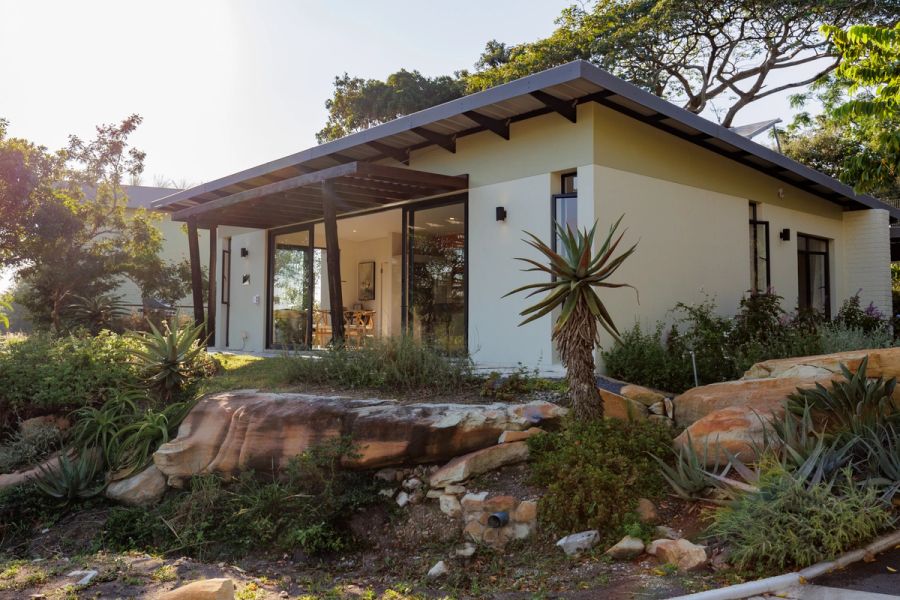 Modern single-storey home exterior with a slanted roof, large sliding doors, and an aloe-planted rock garden in the foreground.