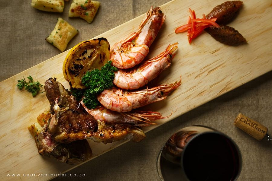 Grilled prawns, lamb chops and charred lemon on a wooden serving board with a glass of red wine, restaurant food photography in Margate