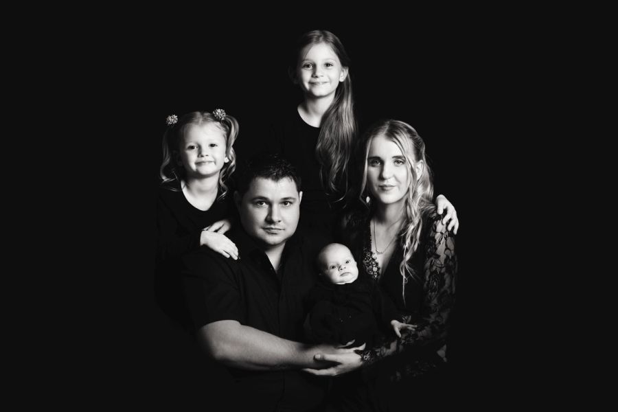 Black and white studio portrait of a family of five, parents with three young children, against a dark background.