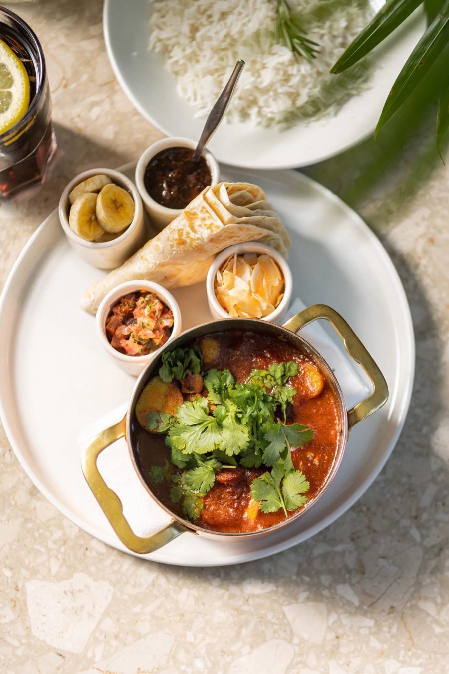 Overhead view of curry in a copper pot with roti, rice and sambals on a marble table at Tashas, Durban