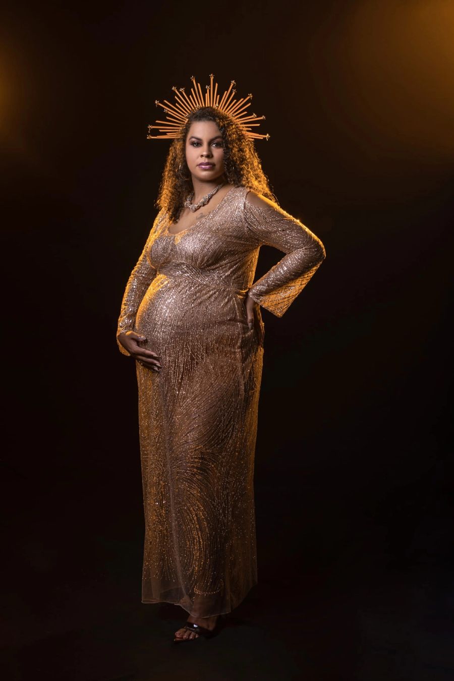 Expectant mother in a sparkling gold sequinned gown and golden crown, lit against a dark studio backdrop, Studio 039, Sea Park.
