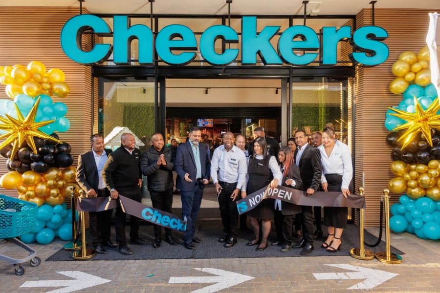 Group of staff and dignitaries cutting a ribbon at a Checkers store opening event under the illuminated storefront sign.