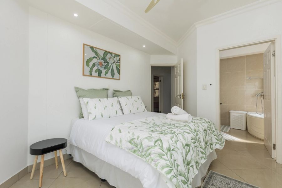 Bright bedroom with a double bed, green leaf-pattern linen, and an en-suite bathroom visible through an open door.