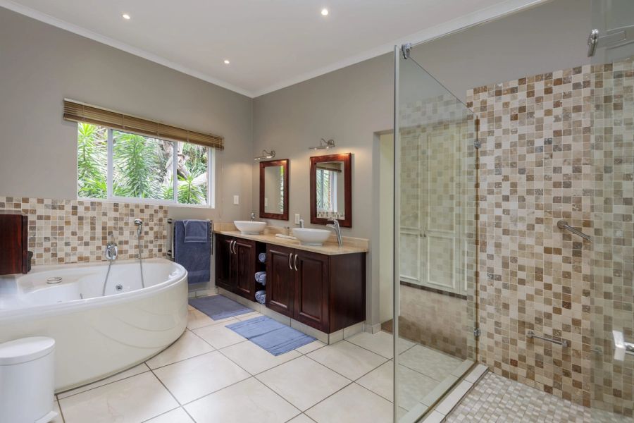Spacious main bathroom with a corner spa bath, double vessel basins and a glass walk-in shower, Southbroom.