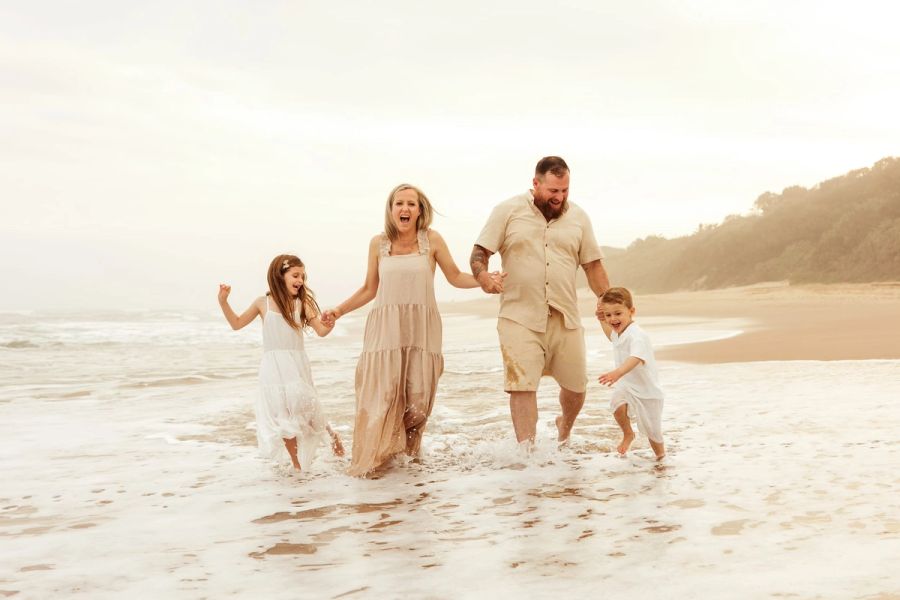 Family of four running hand in hand through the waves at sunset, Trafalgar, KZN South Coast