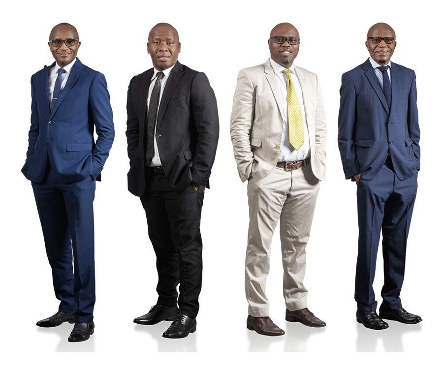 Four businessmen in suits standing side by side against a white studio background.