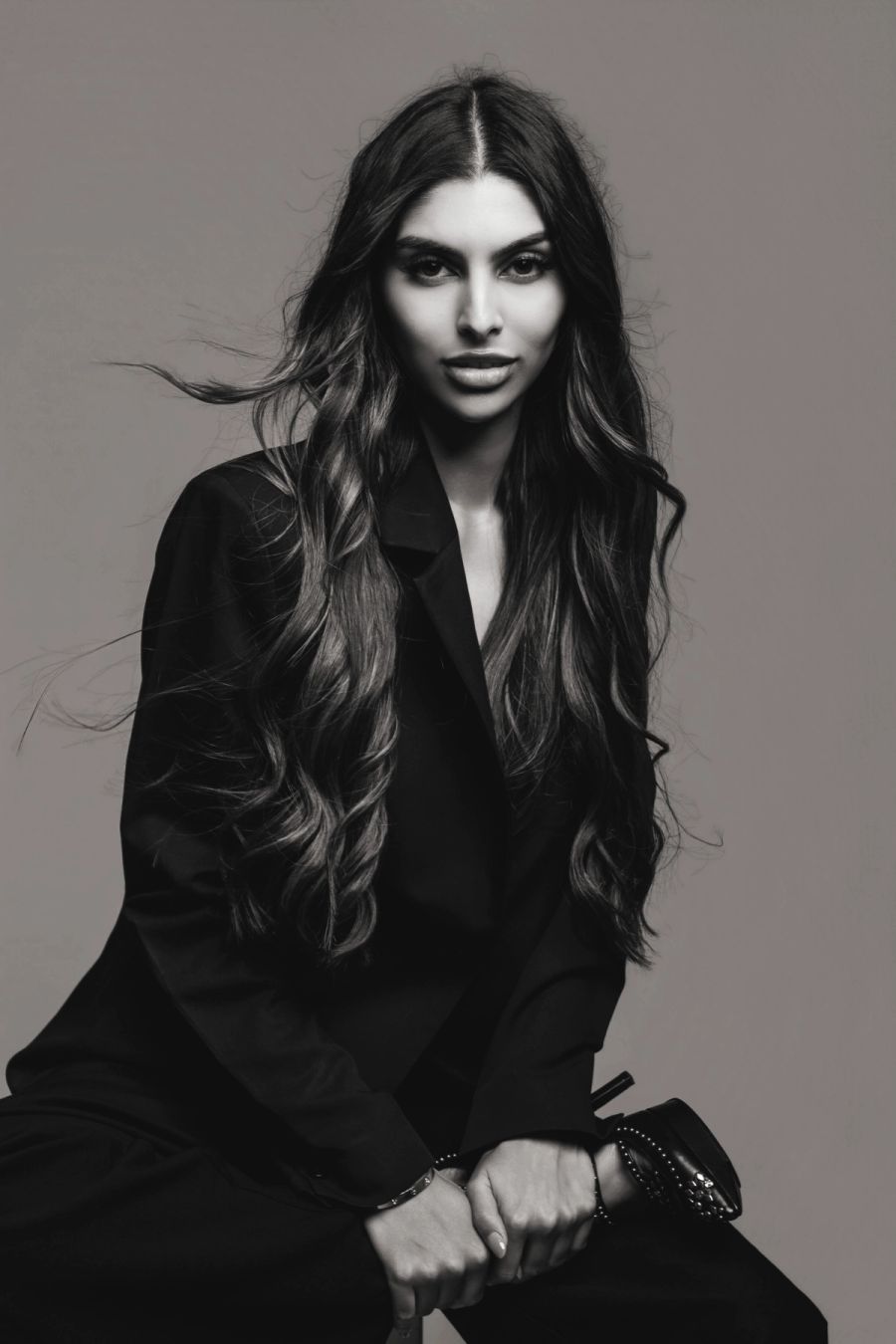 Black and white studio fashion portrait of a woman in a black blazer with long wavy hair.