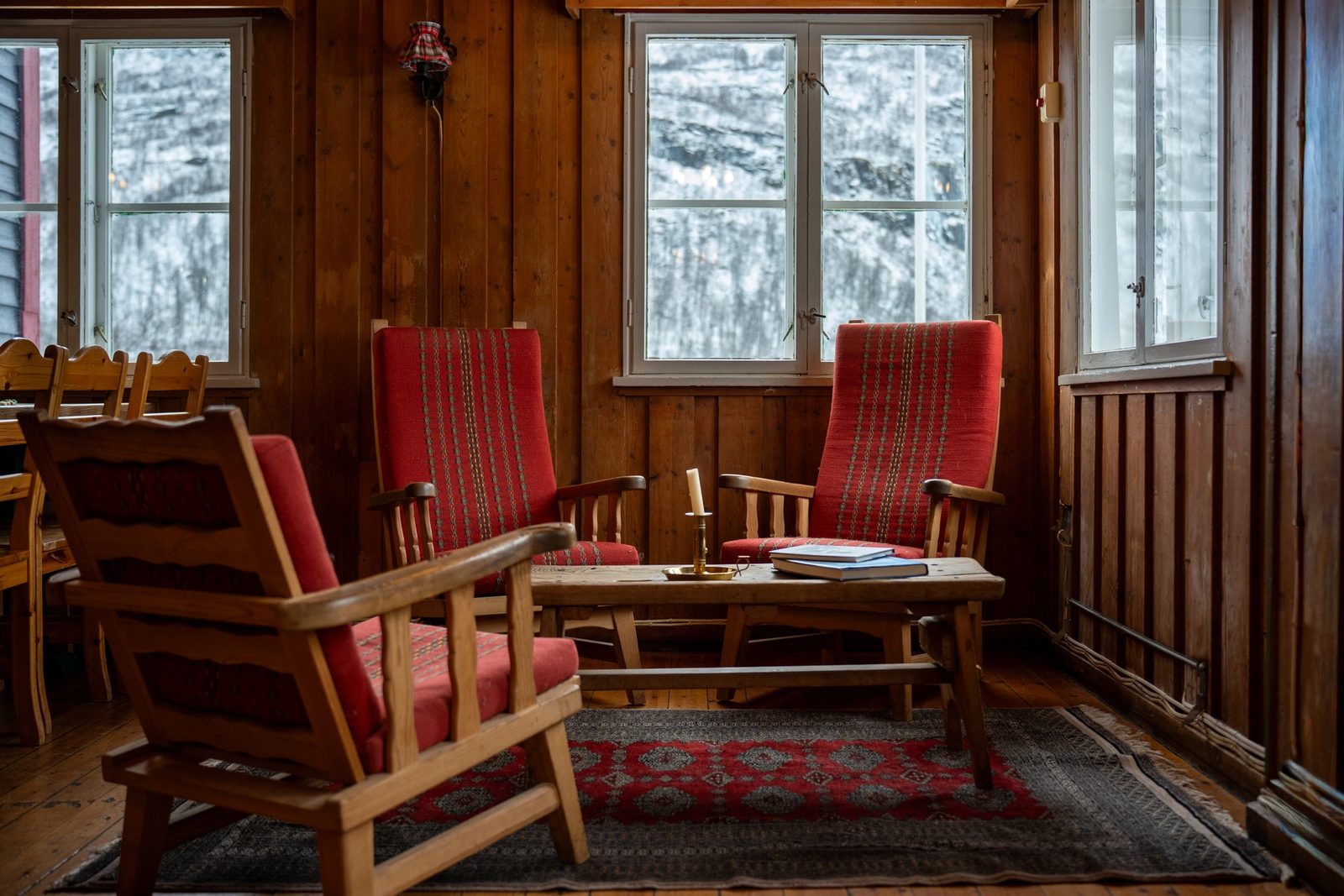 Rustic room with wooden walls, red armchairs, and a snowy winter view from windows.