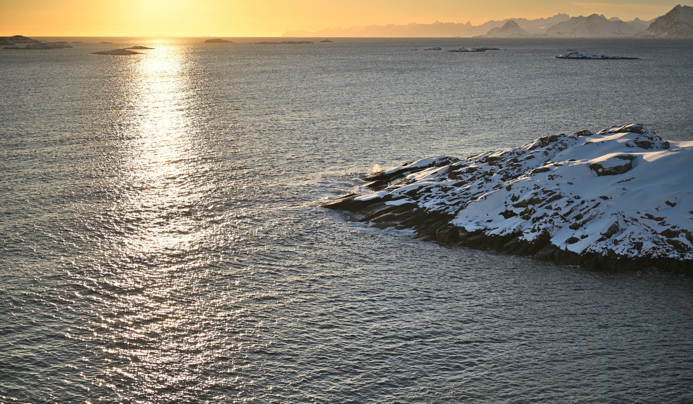 A view over the Arctic Ocean in Lofoten Norway at sunset with snow covered peaks in the background