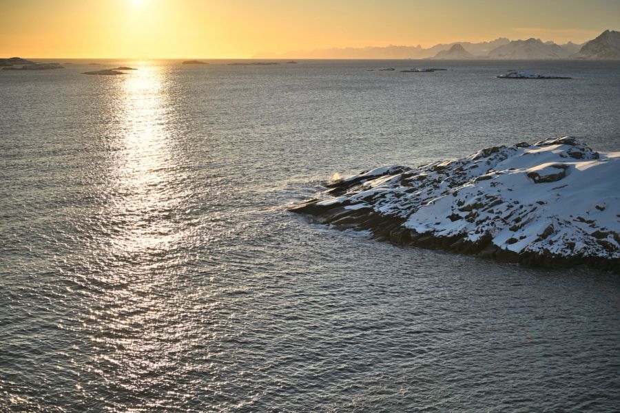 A view over the Arctic Ocean in Lofoten Norway at sunset with snow covered peaks in the background
