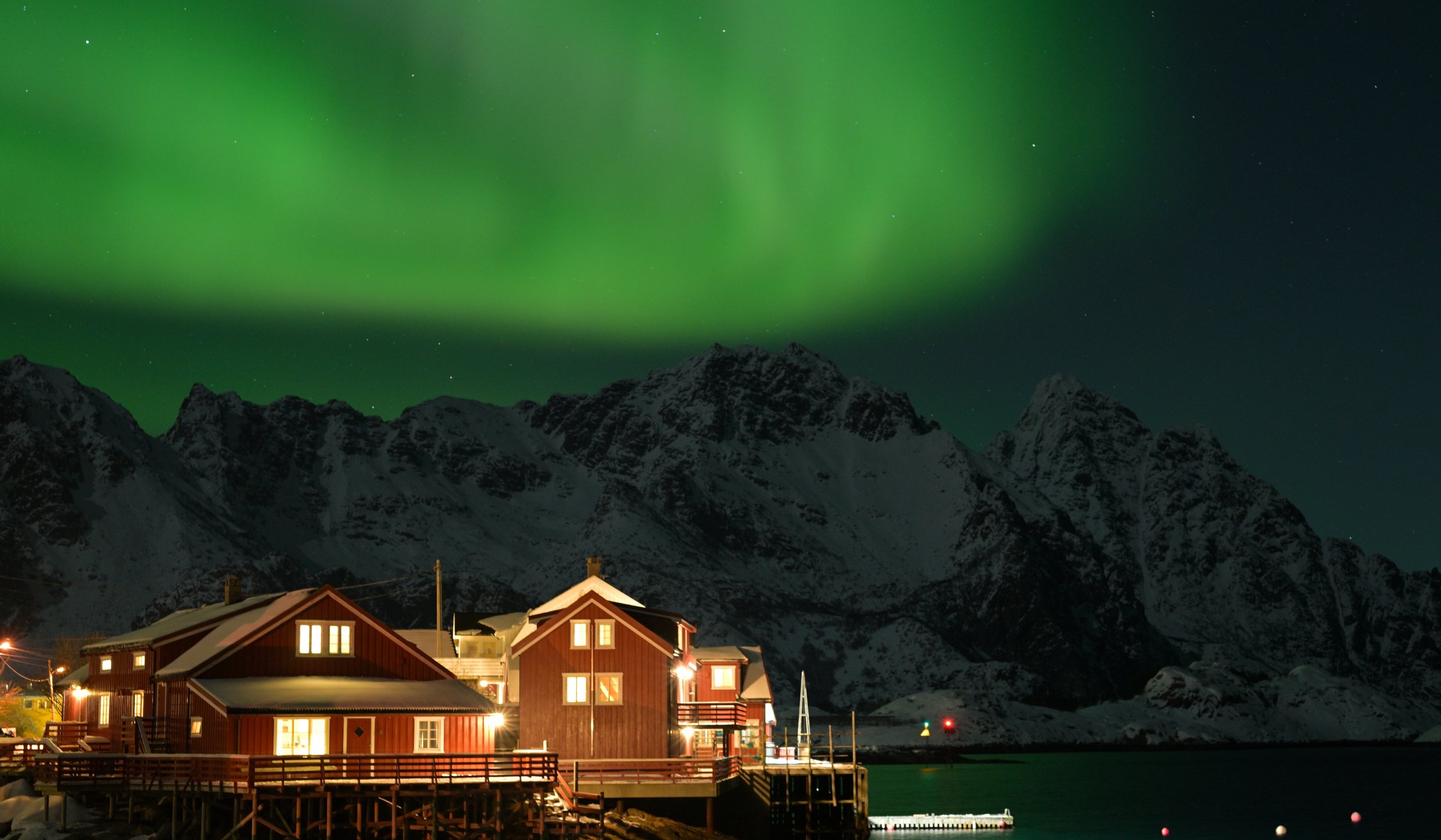 A photo of a waterfront fishermen's cabins with northern lights overhead in Henningsvær Norway