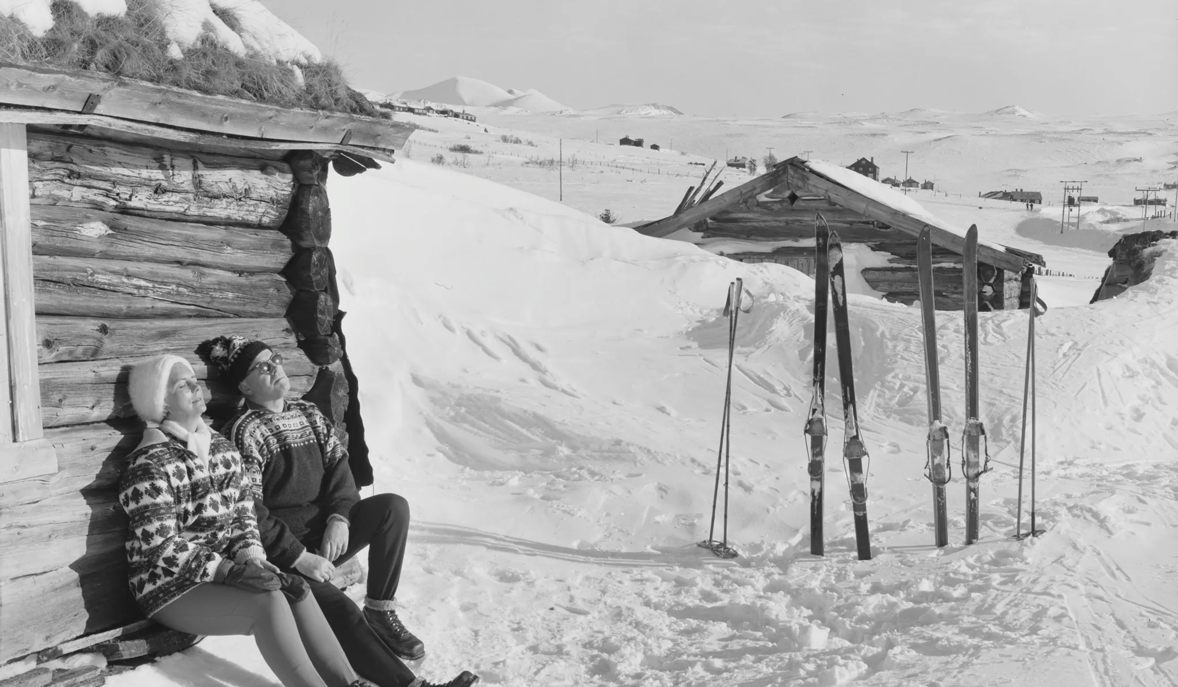 A black and white vintage photo of two skiers relaxing in the mountains