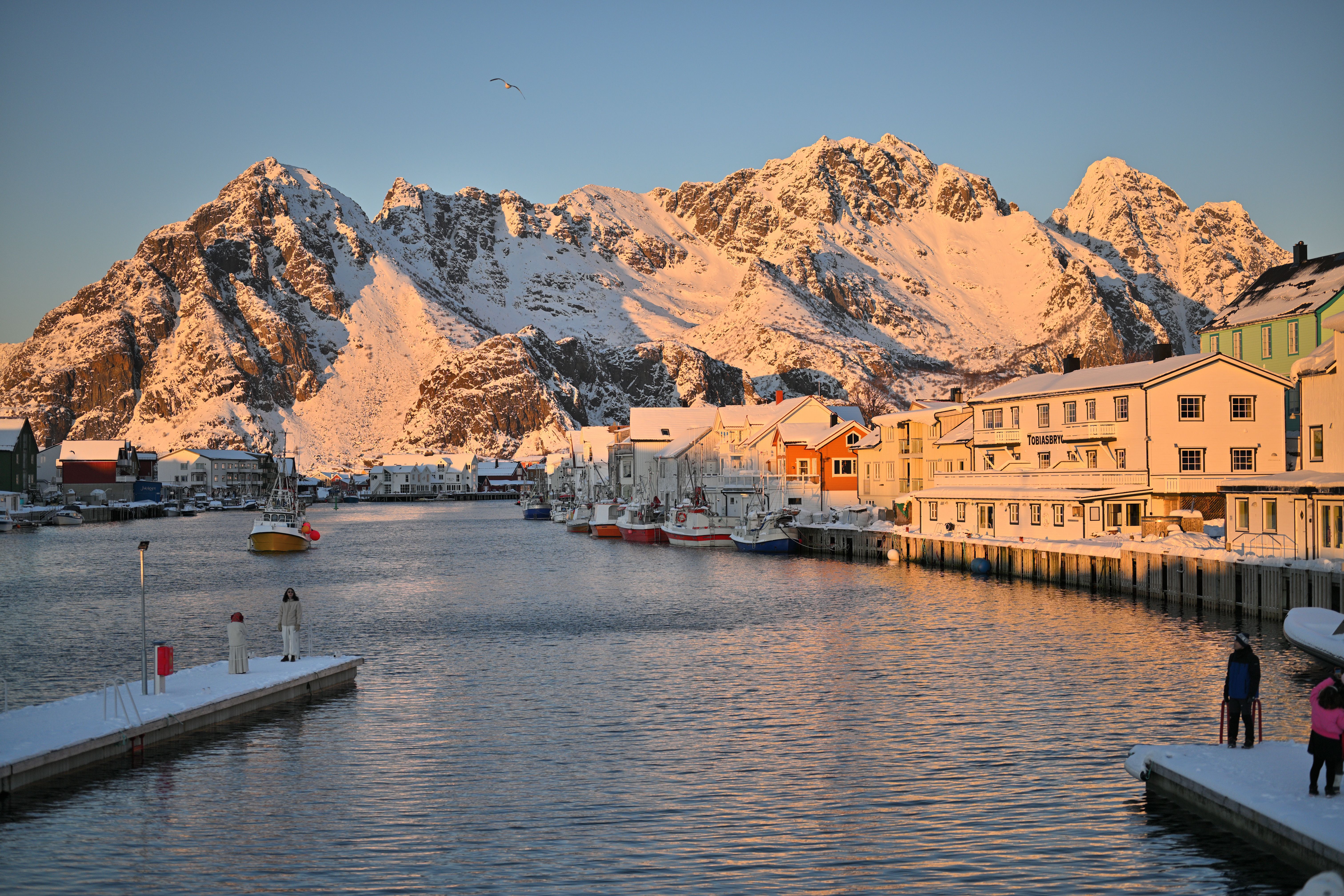 Pier and waterfront wharf buildings covered in snow in the mountains of Henningsvær Norway with snow covered mountains in the background