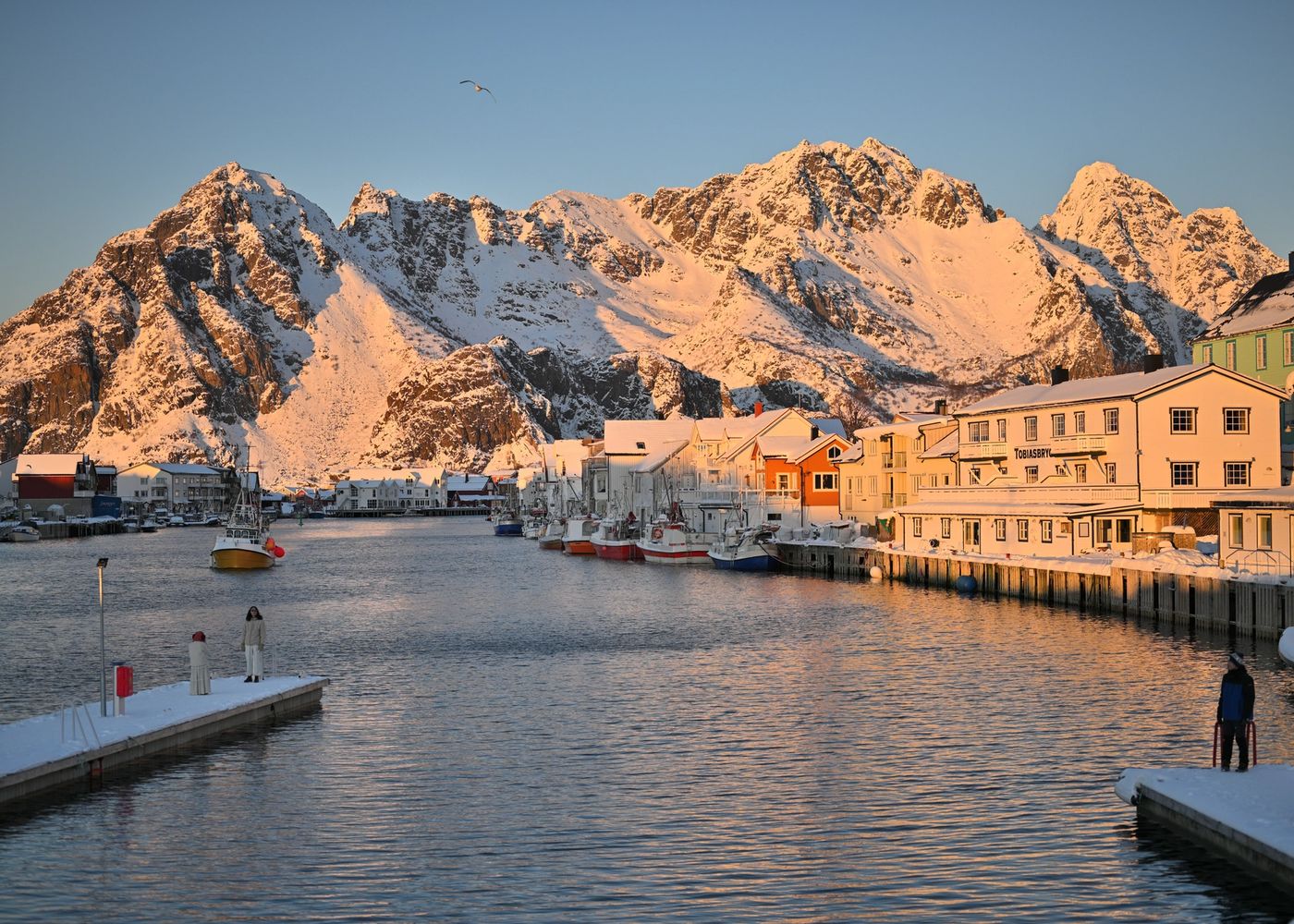 Pier and waterfront wharf buildings covered in snow in the mountains of Henningsvær Norway with snow covered mountains in the background