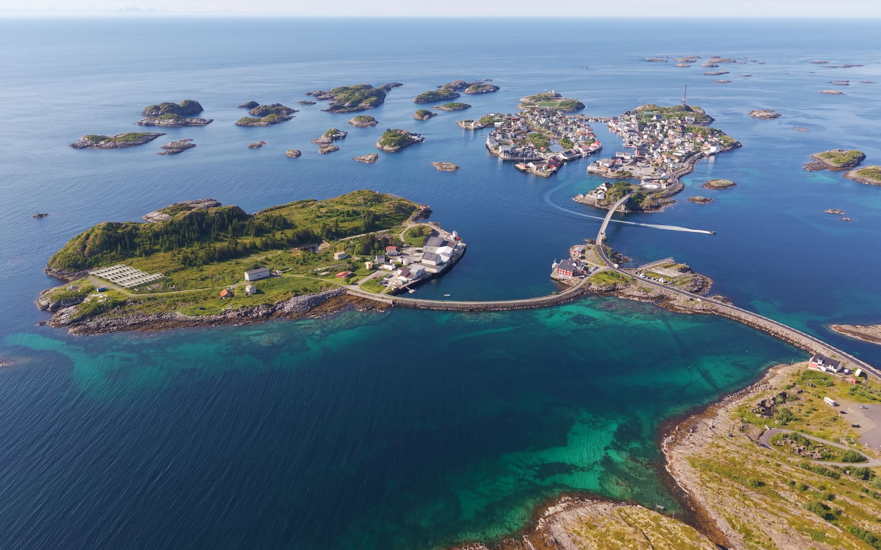 Arctic Coliving - a turquoise lodge on the water in Henningsvær, Norway with mountains in the background.