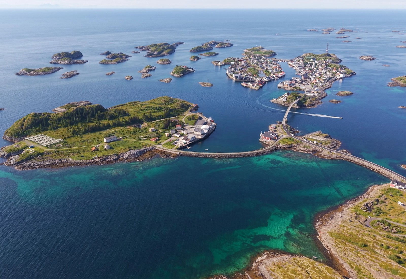 Arctic Coliving - a turquoise lodge on the water in Henningsvær, Norway with mountains in the background.
