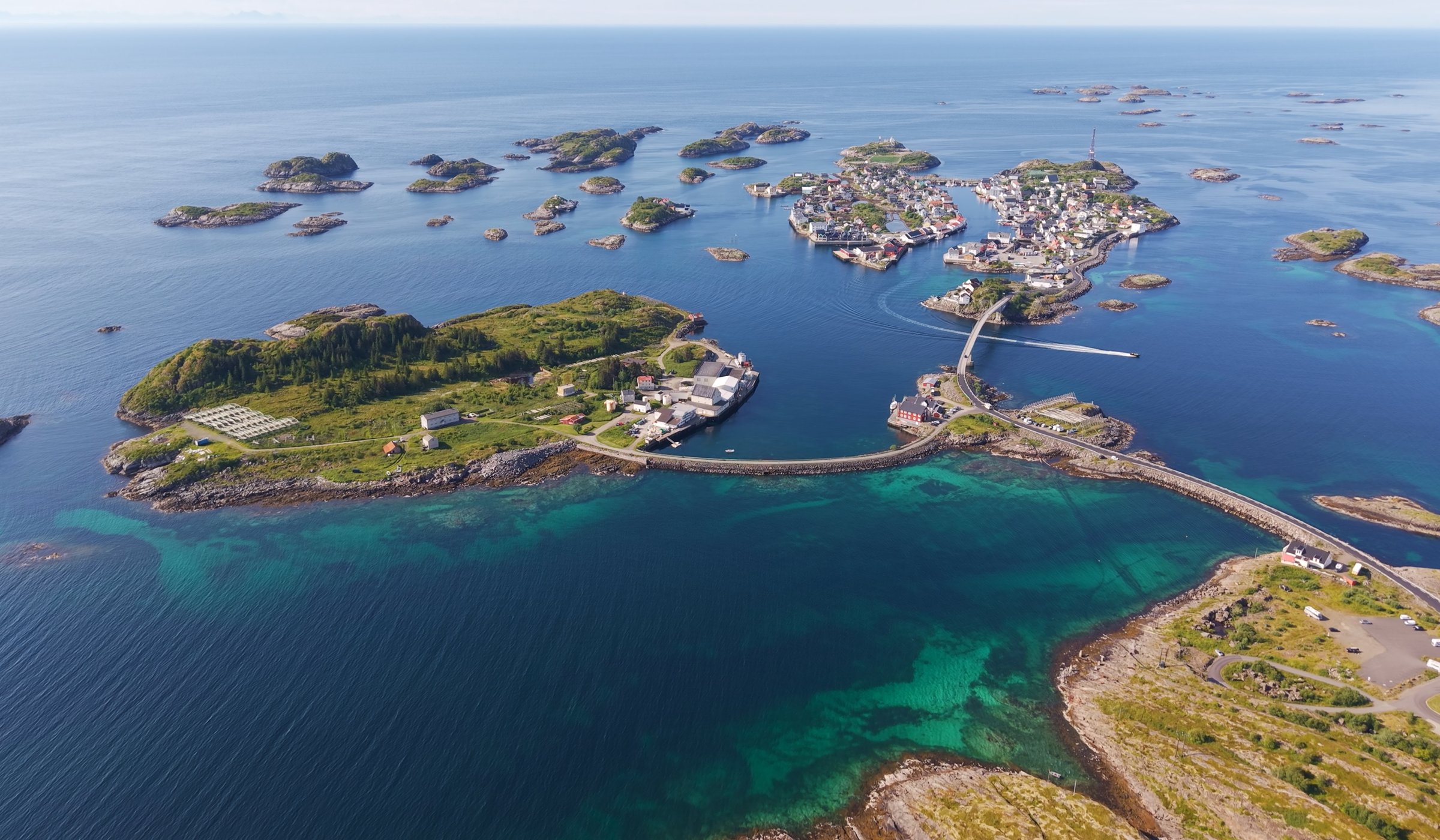 Arctic Coliving - a turquoise lodge on the water in Henningsvær, Norway with mountains in the background.