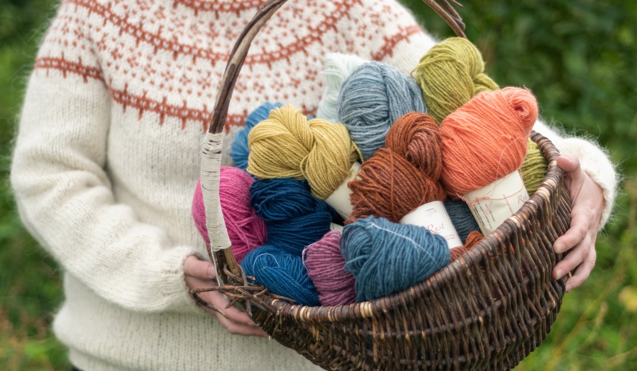 A woman in a traditional cream and orange Norwegian knit carrying a basket of colorful hand-dyed yarn