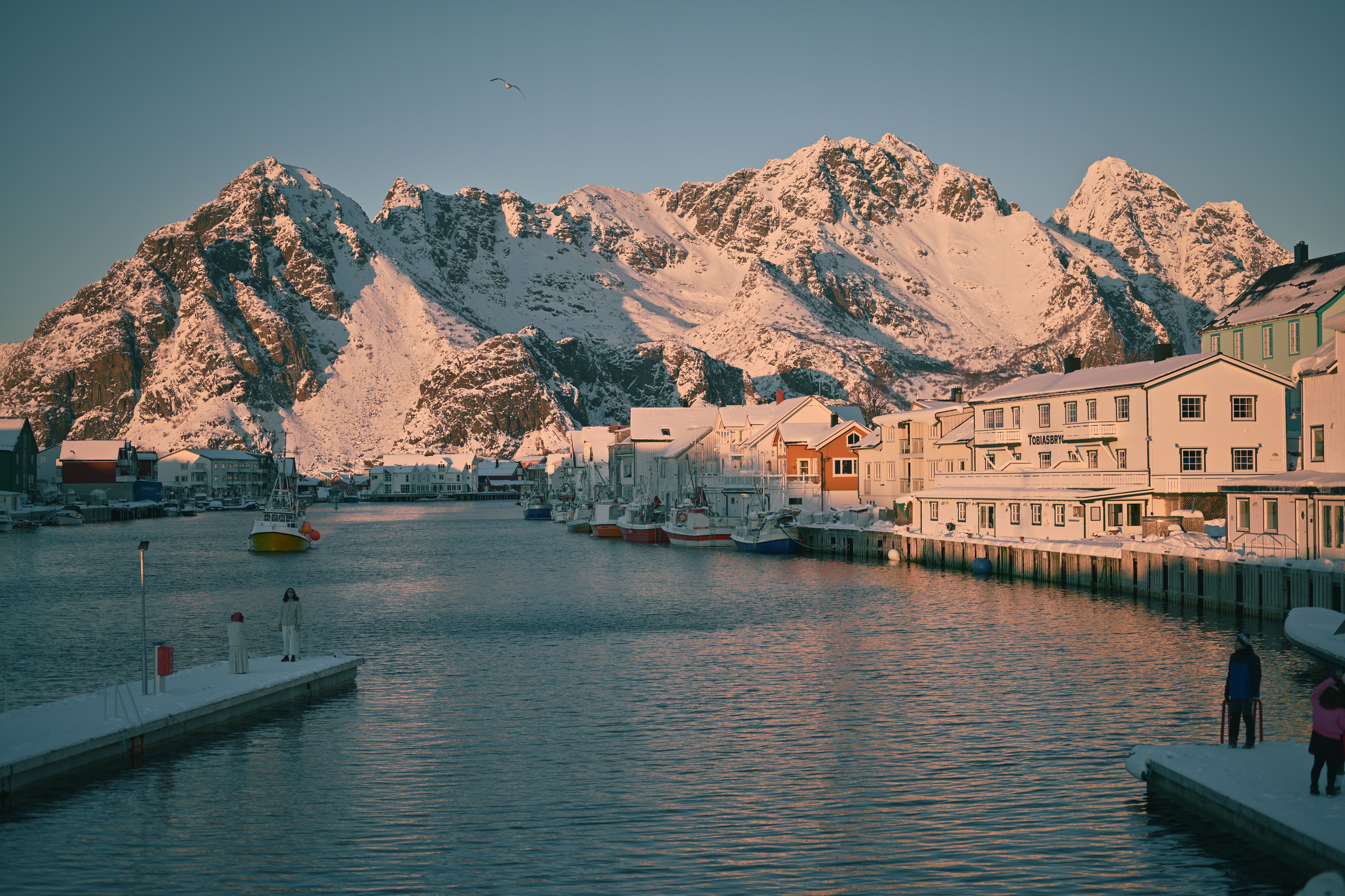 Pier and waterfront wharf buildings covered in snow in the mountains of Henningsvær Norway with snow covered mountains in the background