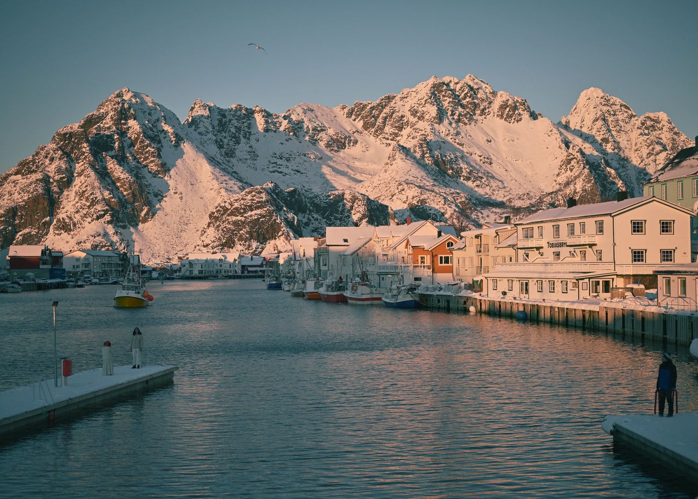 Pier and waterfront wharf buildings covered in snow in the mountains of Henningsvær Norway with snow covered mountains in the background