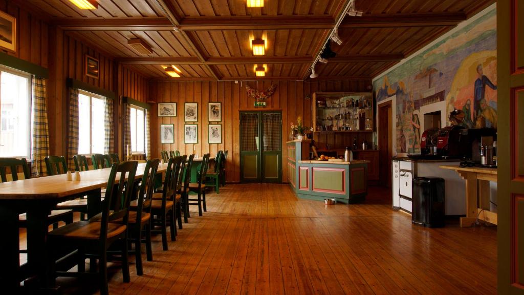 A rustic wooden dining hall with long tables, a bar area, and a colorful mural.