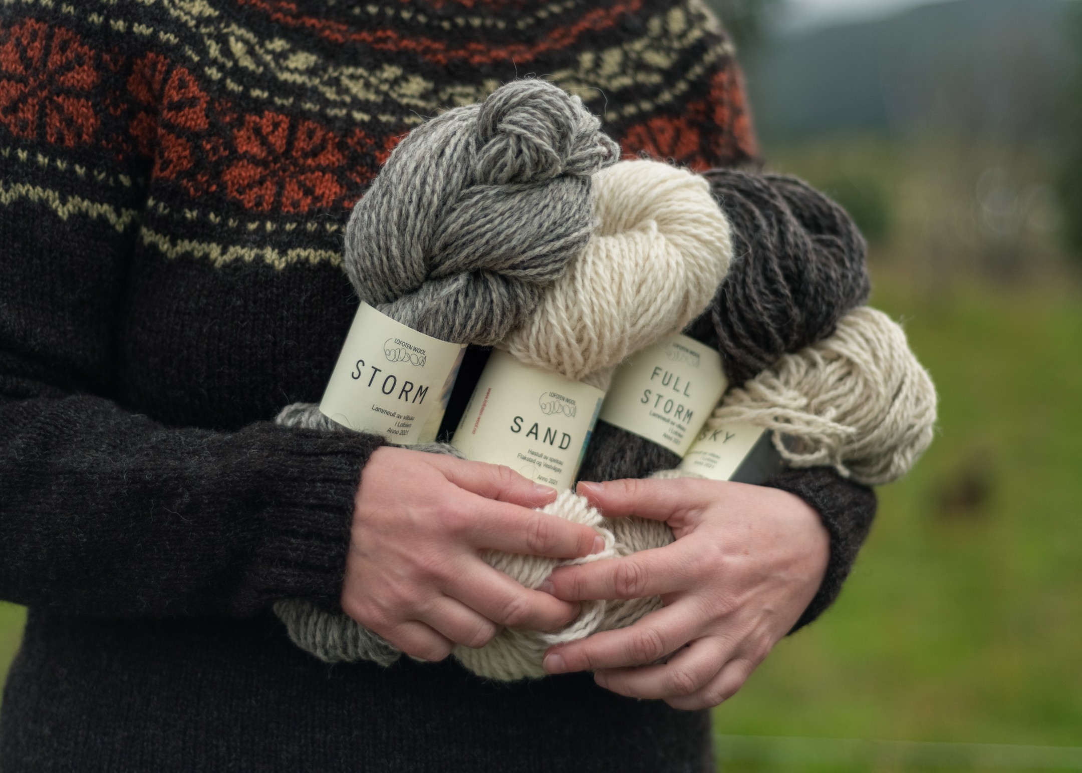 A closeup of a person in a Norwegian sweater carrying Lofoten Wool Storm and Sand yarn