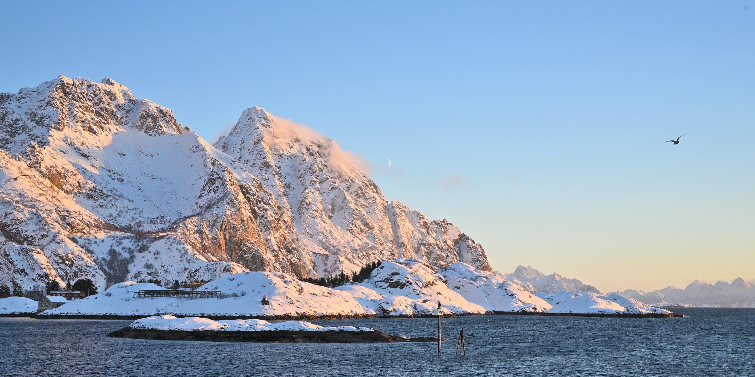 A snowy mountain coastline seen from the town of Henningsvær Norway in the early winter twilight