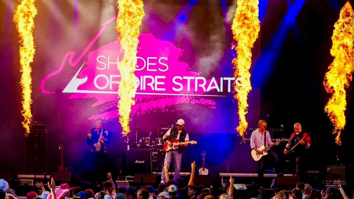 Fire menn på en scene som spiller på instrumenter med pyro.