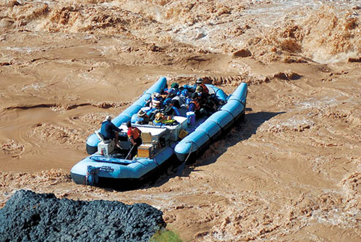 A large blue Demaree inflatable boat travels down the muddy Colorado River. 