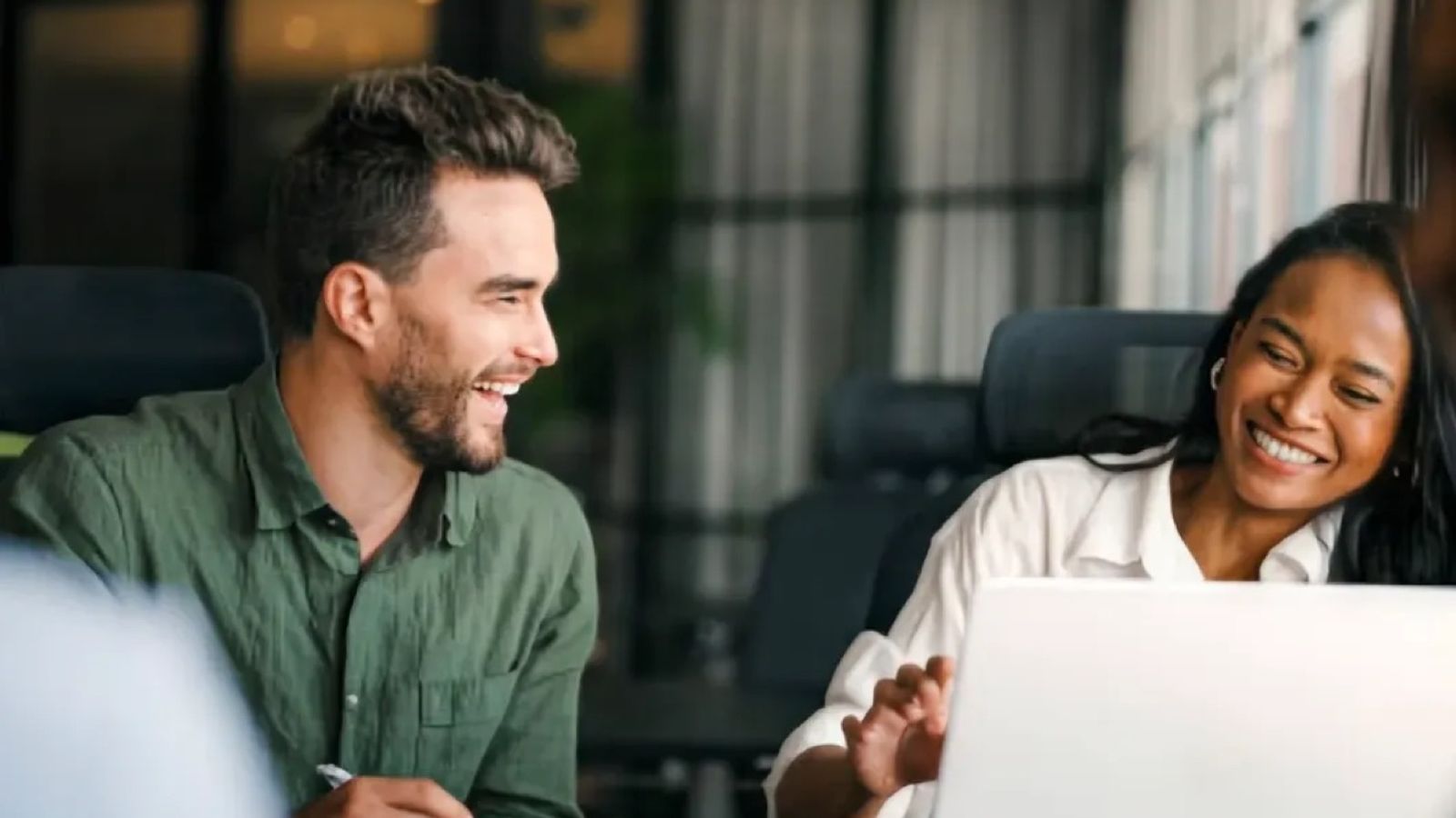 Two colleagues laughing as they work on laptops