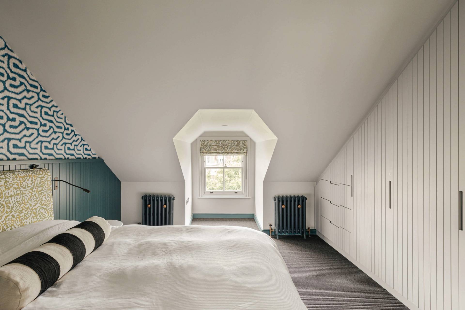 Spacious attic bedroom with sloped ceilings, dormer sash window, and dark radiators, Love Locations.