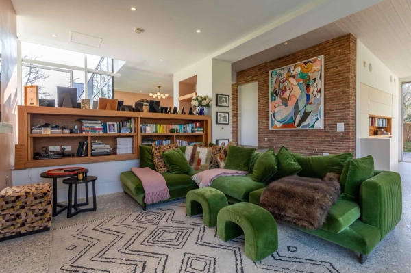 Love Locations eclectic living room location Godalming: Cozy lounge corner featuring a deep green velvet sectional couch and an authentic exposed brick accent wall, tailored for drama filming.