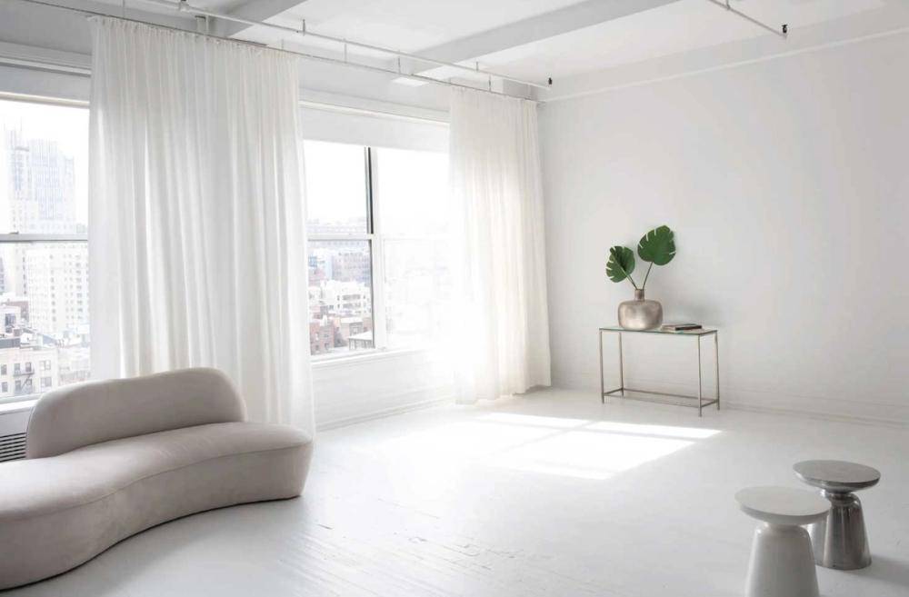 Sunlit studio window corner in New York, NY 10011 showing white sheer curtains, a minimalist armchair, and polished floors, perfect for lifestyle brand advertising, Love Locations.