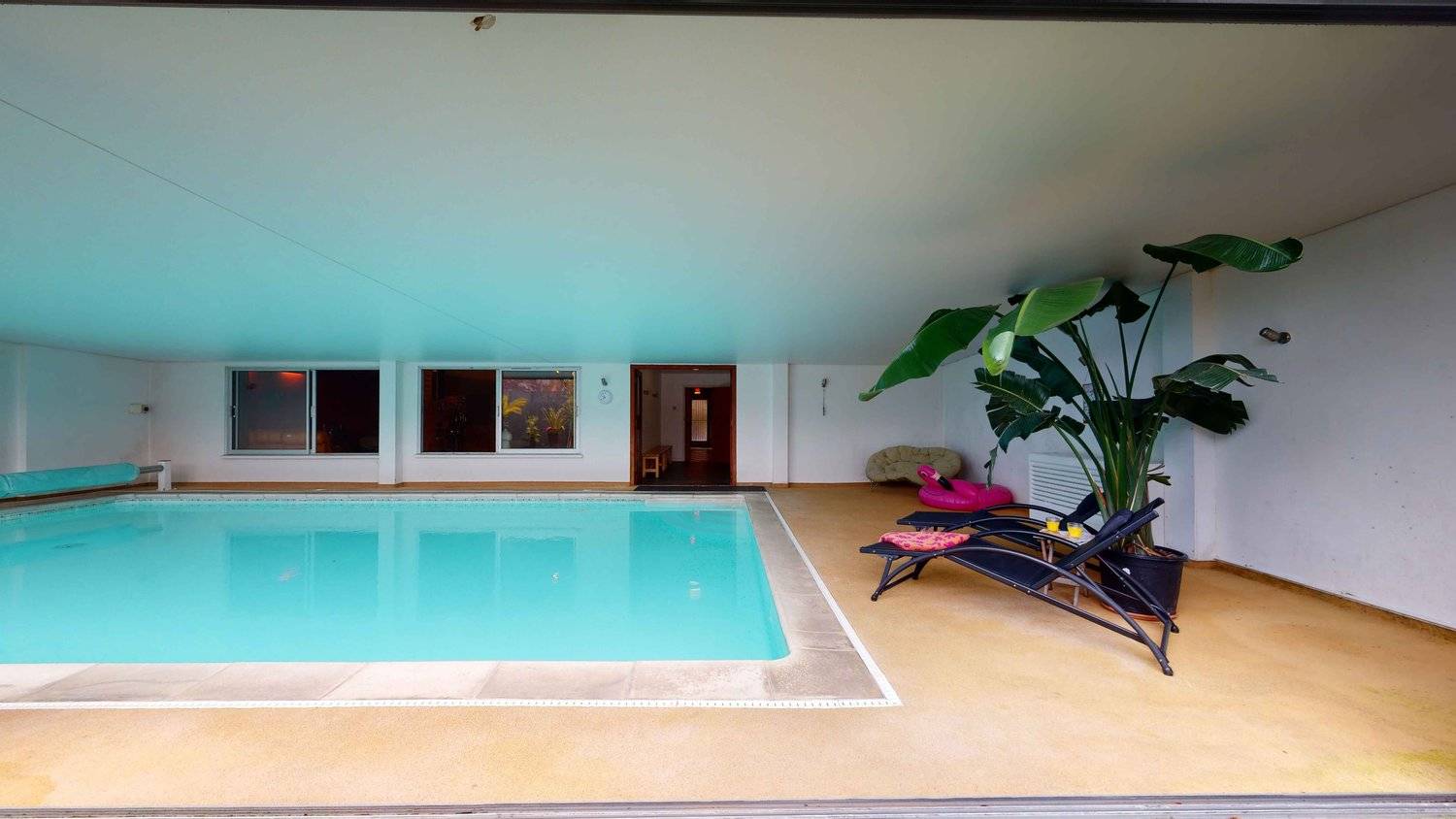 Indoor swimming pool area with retro sun loungers, tropical house plants, and blue ceilings in SW16, Love Locations.