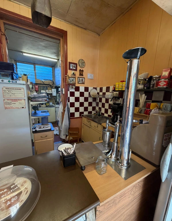 Retro cafe service counter behind-the-scenes view with coffee equipment, checkered wall tiles, and food prep counters, Love Locations SE27.