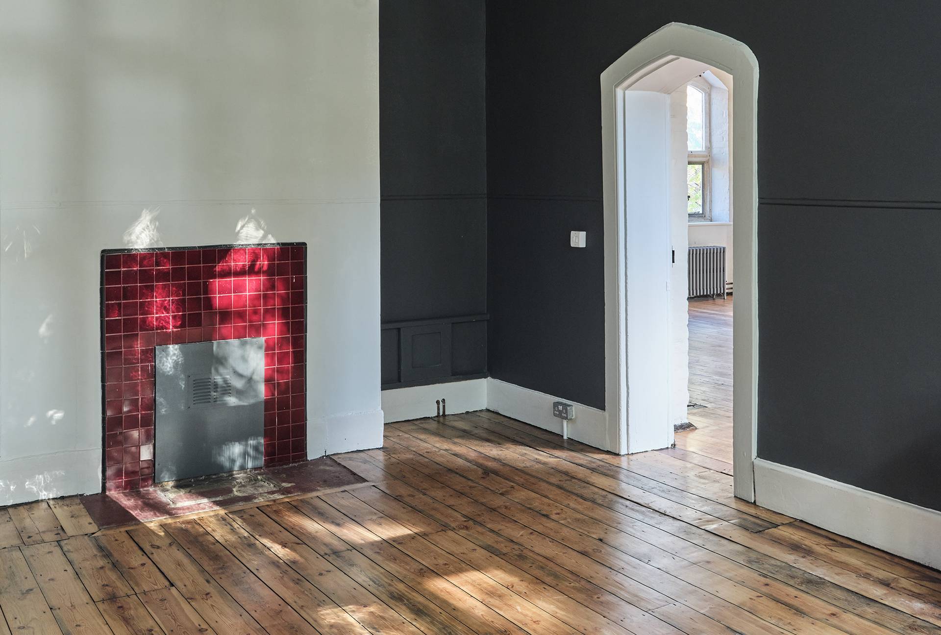 Dark green panelled room with a red tiled fireplace hearth and open doorway transition, perfect for dramatic film scenes, Love Locations E2.