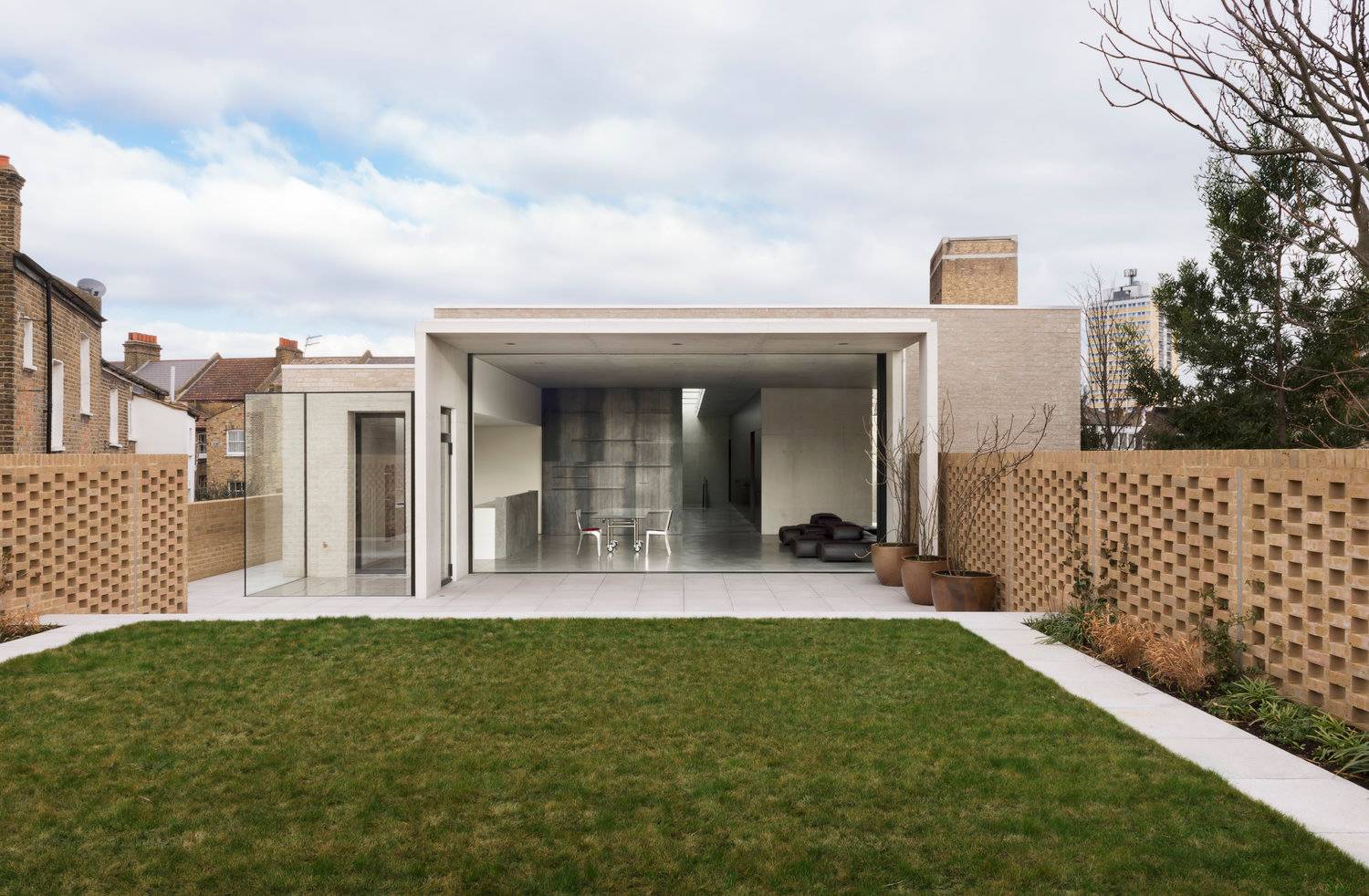 Rear architectural elevation of a modern brutalist home showing full-width glass sliding doors opening to a neat lawn, the ultimate backdrop for luxury car and tech brand commercials via Love Locations.