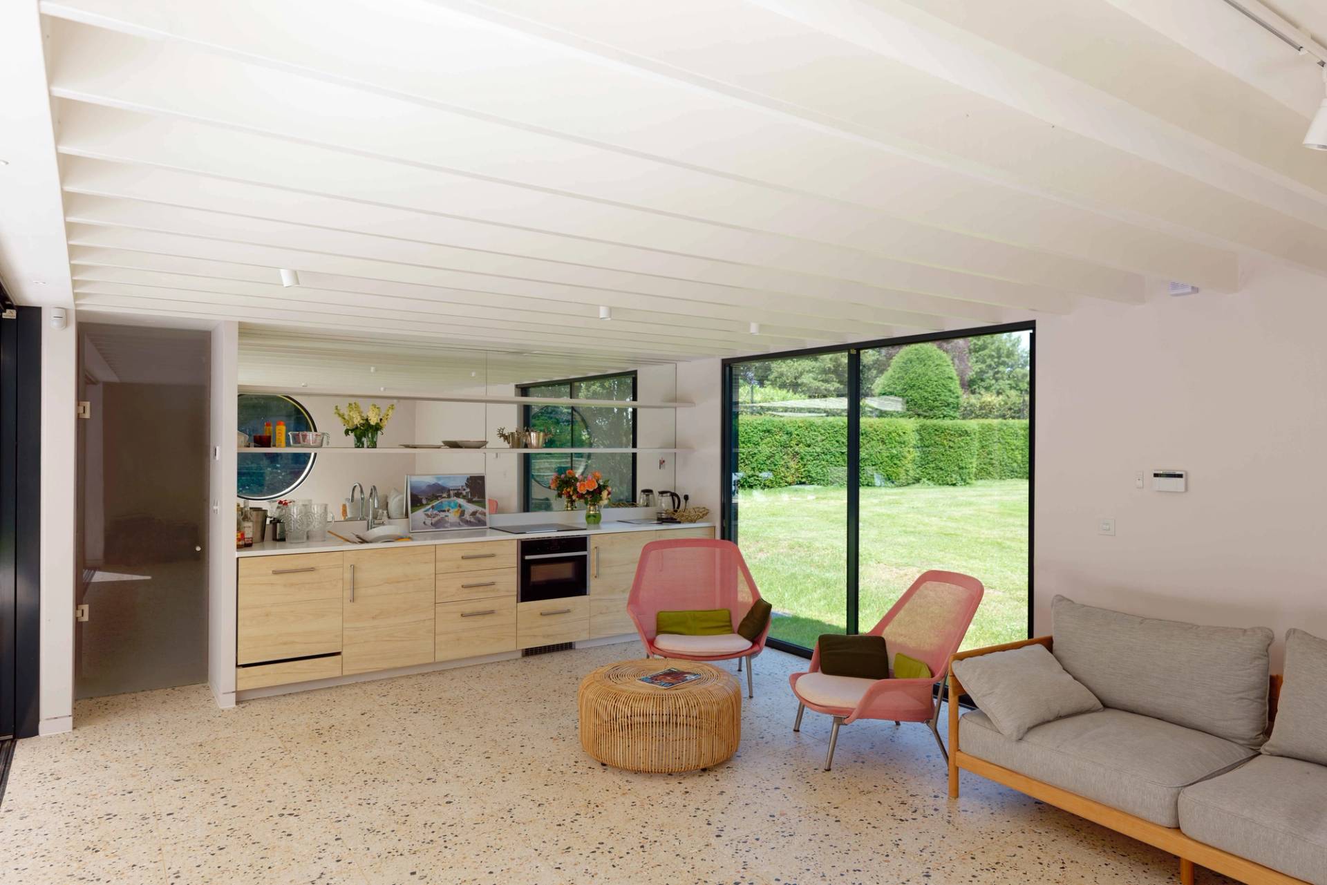 Open-plan pool house interior with light plywood kitchen, pink lounge chairs, and terrazzo floors, Love Locations OX7.