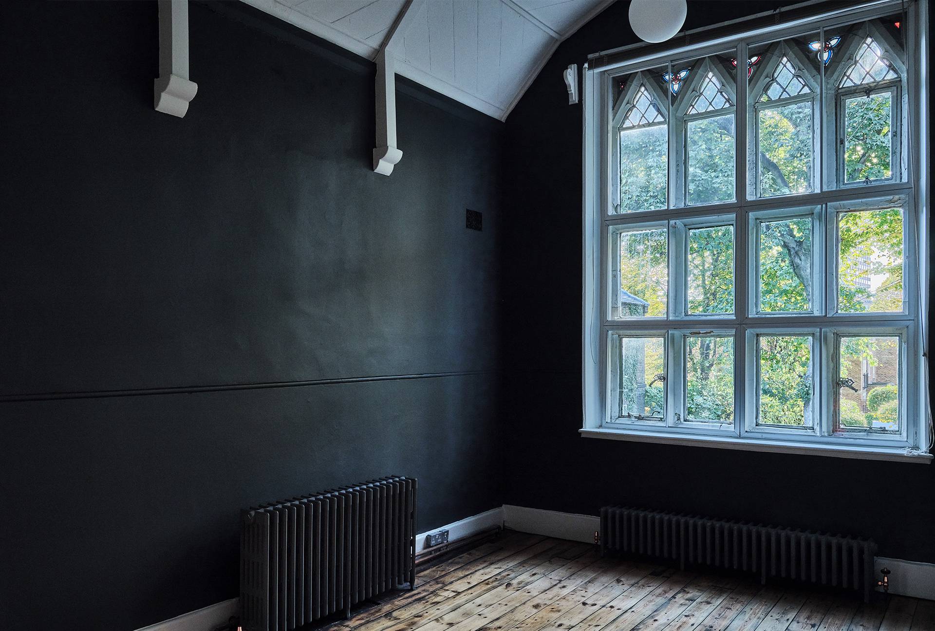Cozy dark green painted snug room featuring arched windows, dark radiators, and wooden floorboards, Love Locations.