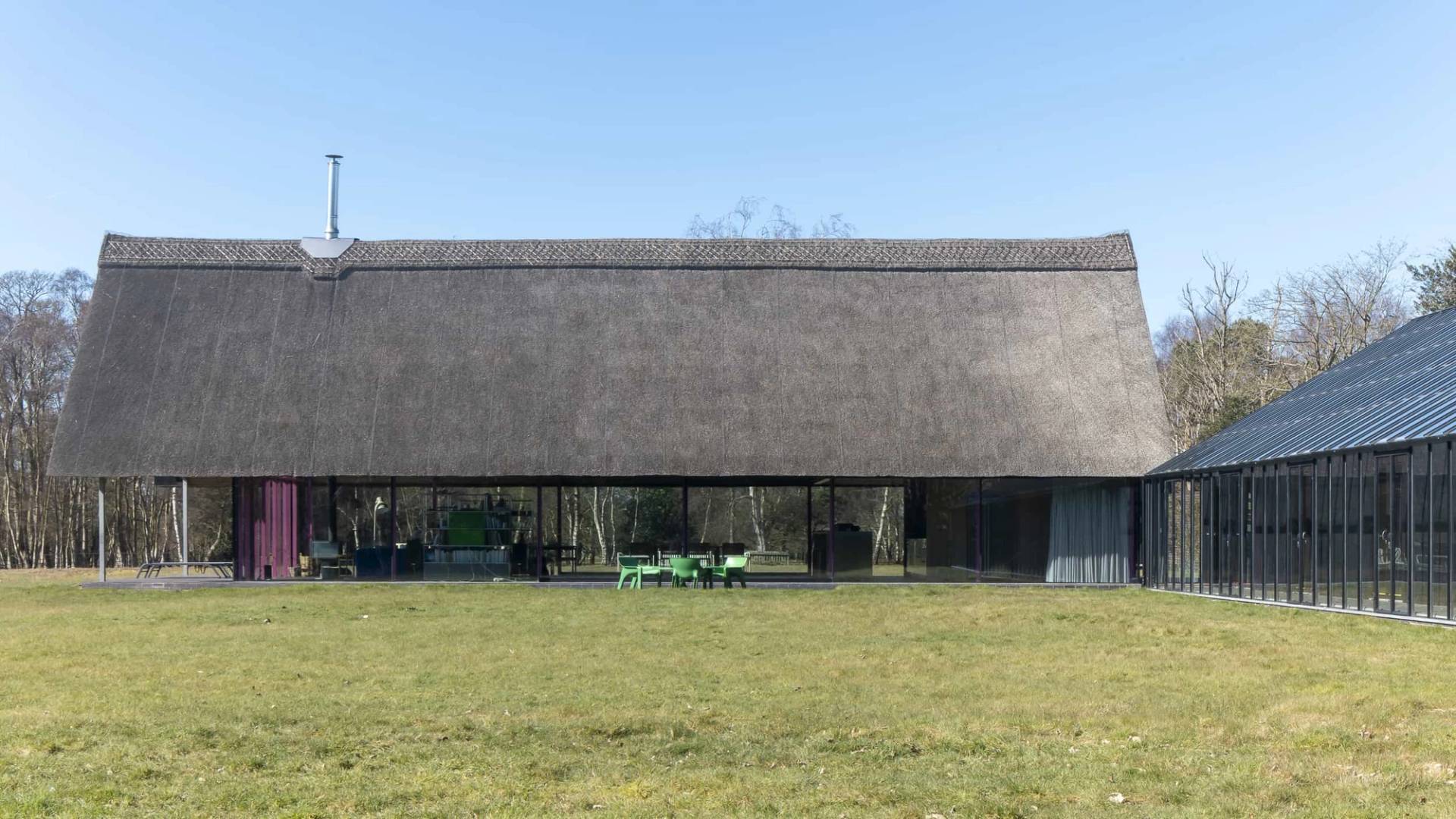 Side elevation of a modern thatched longhouse with full-height glass walls and dark roof, Love Locations IP17.
