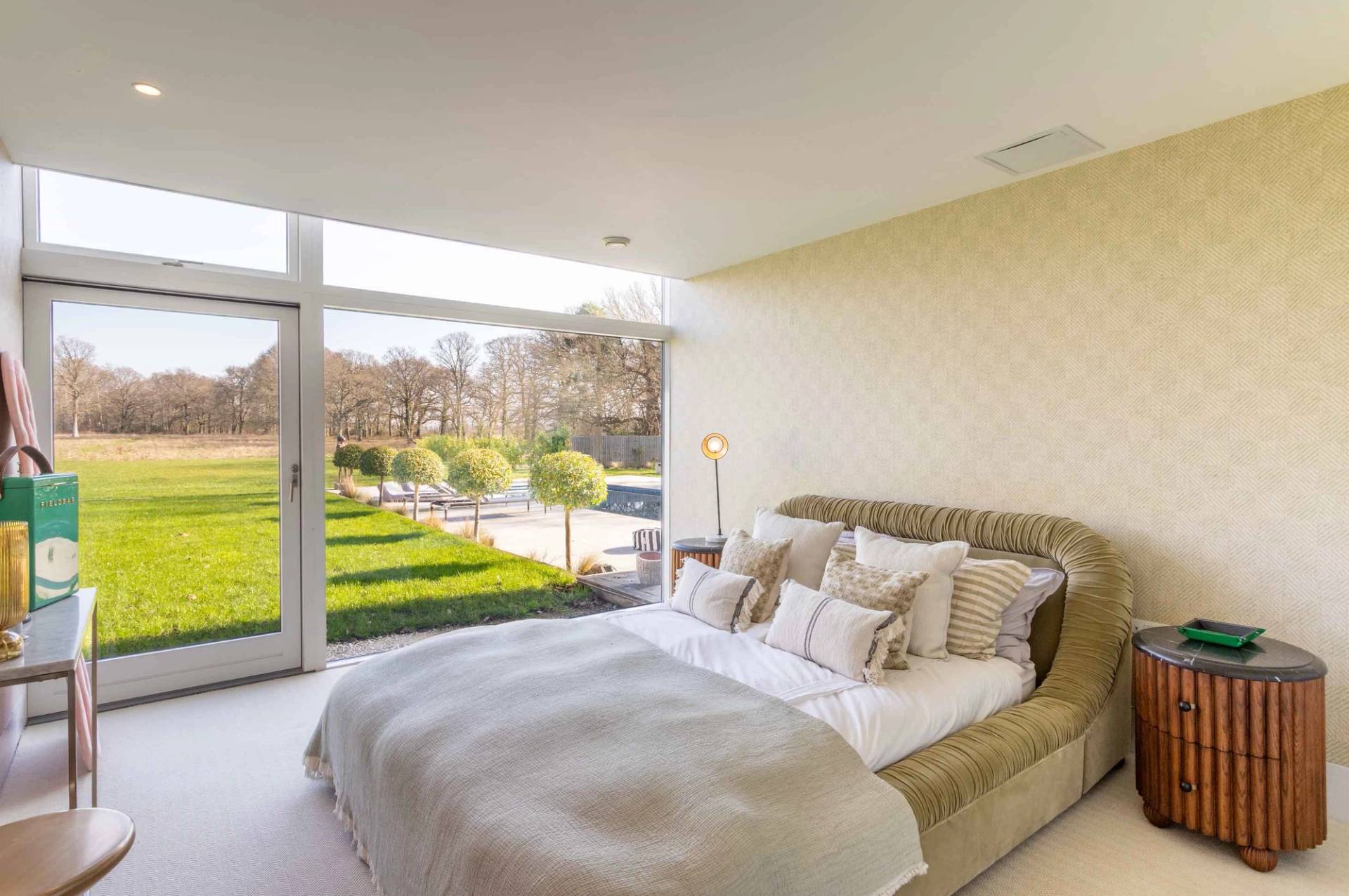 Love Locations elegant family home GU8: Neutral toned guest bedroom with a wide sliding glass door framing garden courtyard views, ideal for lifestyle branding shoots.
