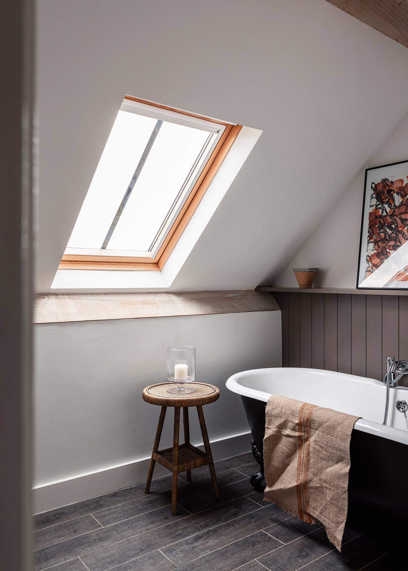 Attic bathroom set under a skylight window featuring a black roll-top bathtub and wooden stool, Love Locations SN8.