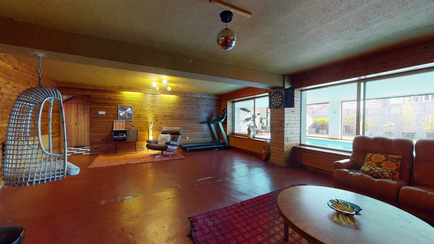 Retro 1970s games lounge with red floor finish, treadmill, vintage armchairs, and timber panelled walls, Love Locations SW16.