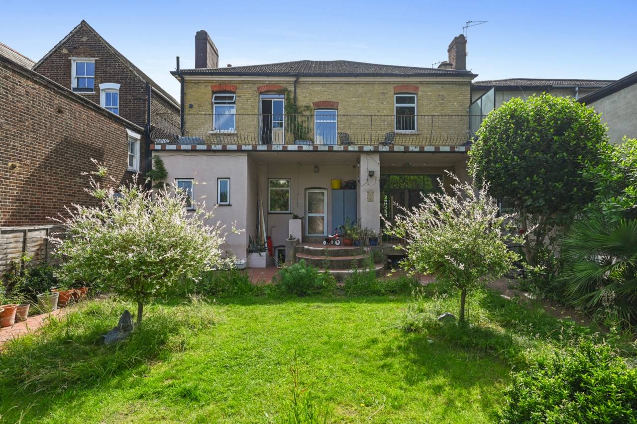 Rear elevation of a yellow brick Victorian location home showing an expansive green lawn garden, Love Locations.