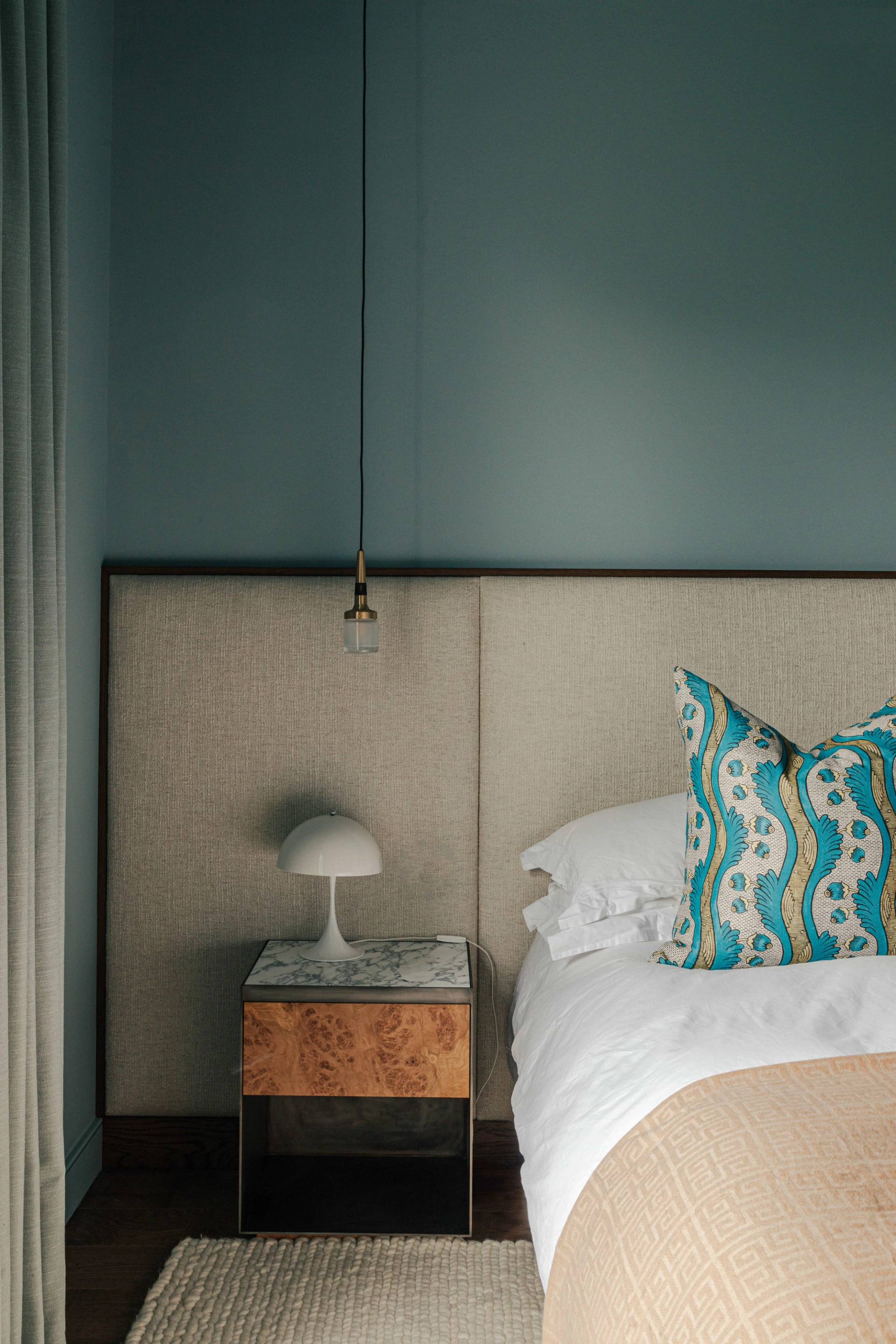 Master bedroom nightstand detail showing a tall upholstered headboard, brass pendant, and marble lamp, Love Locations.
