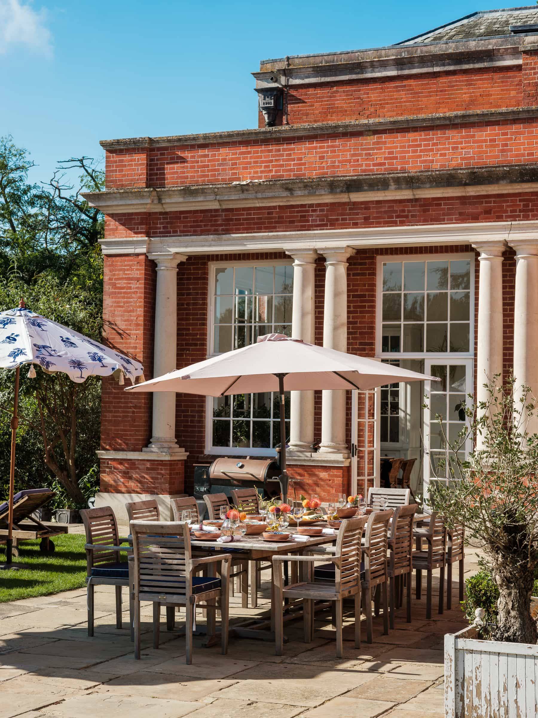 Al fresco patio dining table set outside a red brick Georgian mansion facade with parasols, Love Locations RG42.