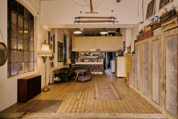 Wide perspective of a historic industrial warehouse loft looking down a long open-plan floor space towards a raised kitchen counter, Love Locations.