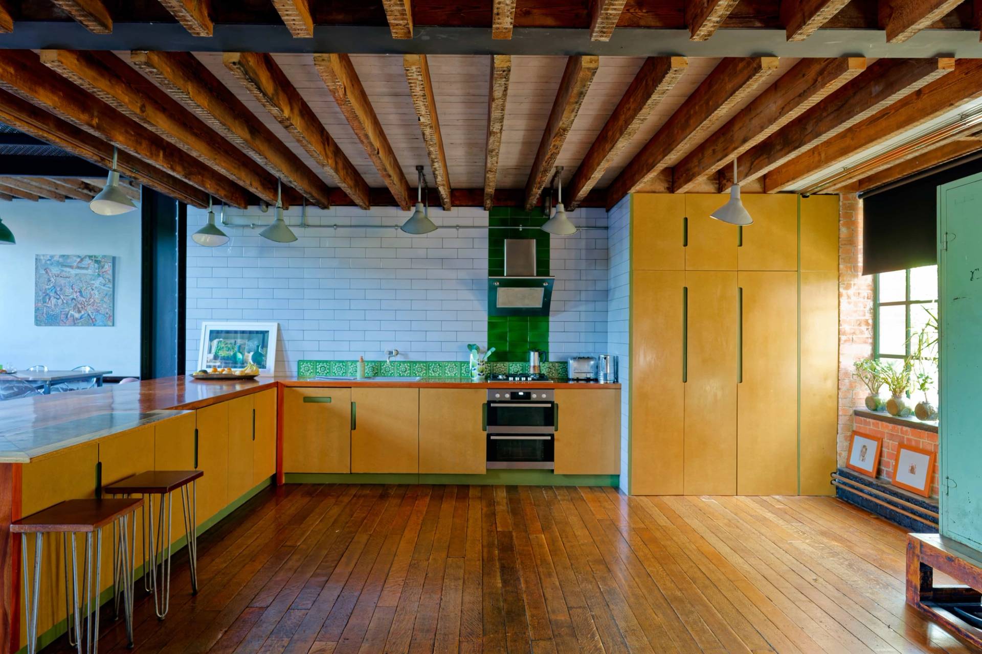 Industrial kitchen featuring a wide timber island counter, yellow cabinetry, tiled splashback, and exposed ceiling joists, ideal for culinary ads, Love Locations.
