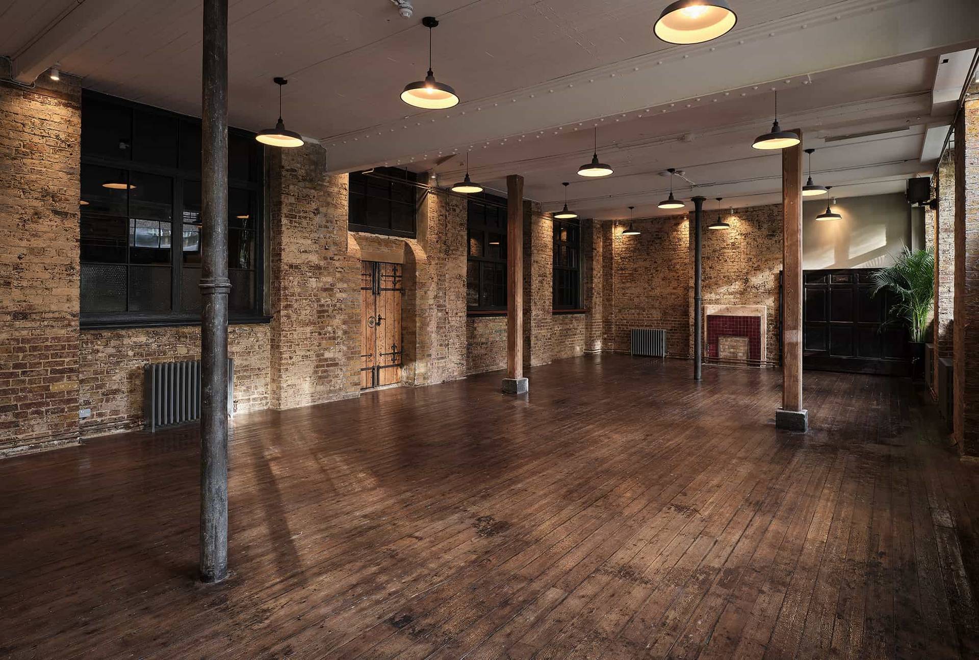 Warehouse event space with exposed brick walls, timber posts, and warm overhead pendant lighting, ideal for pop-up markets, Love Locations E2.