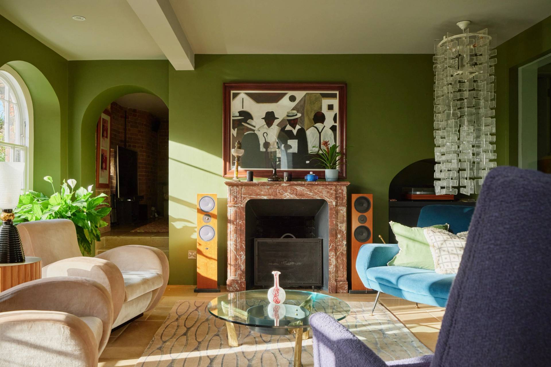 Olive green reception room featuring an open fireplace, abstract art, and blue velvet armchairs, Love Locations.